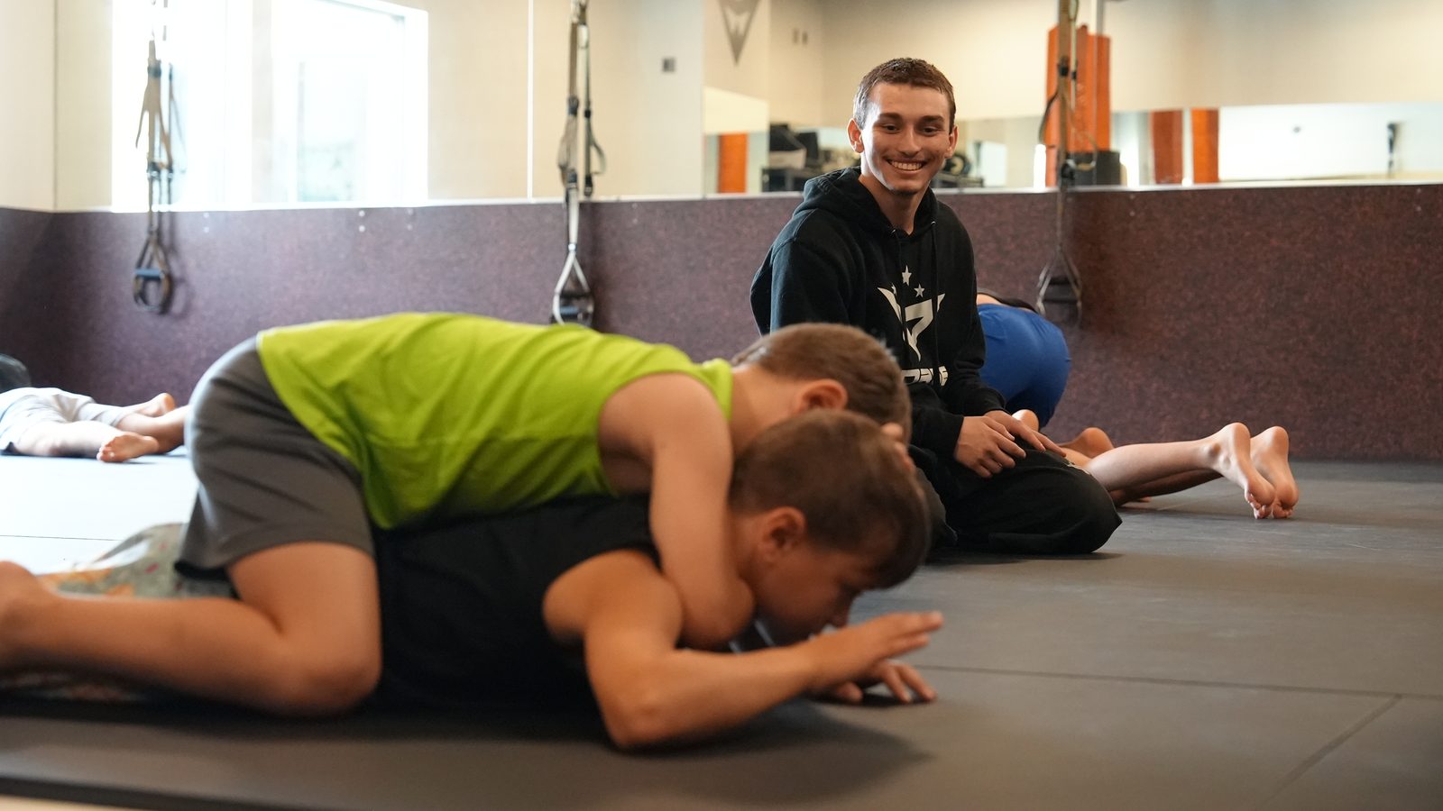 A coach watches two young students work a grappling drill on the mat at Forge Athletics in Naples