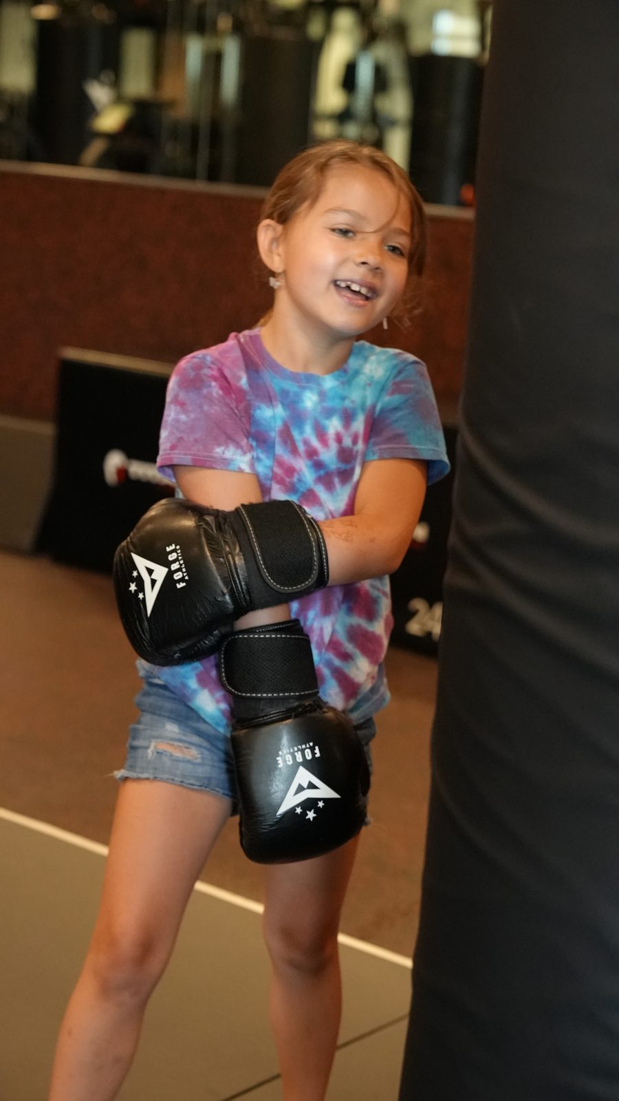 A young Little Dragons student smiles in her boxing gloves at Forge Athletics in Naples