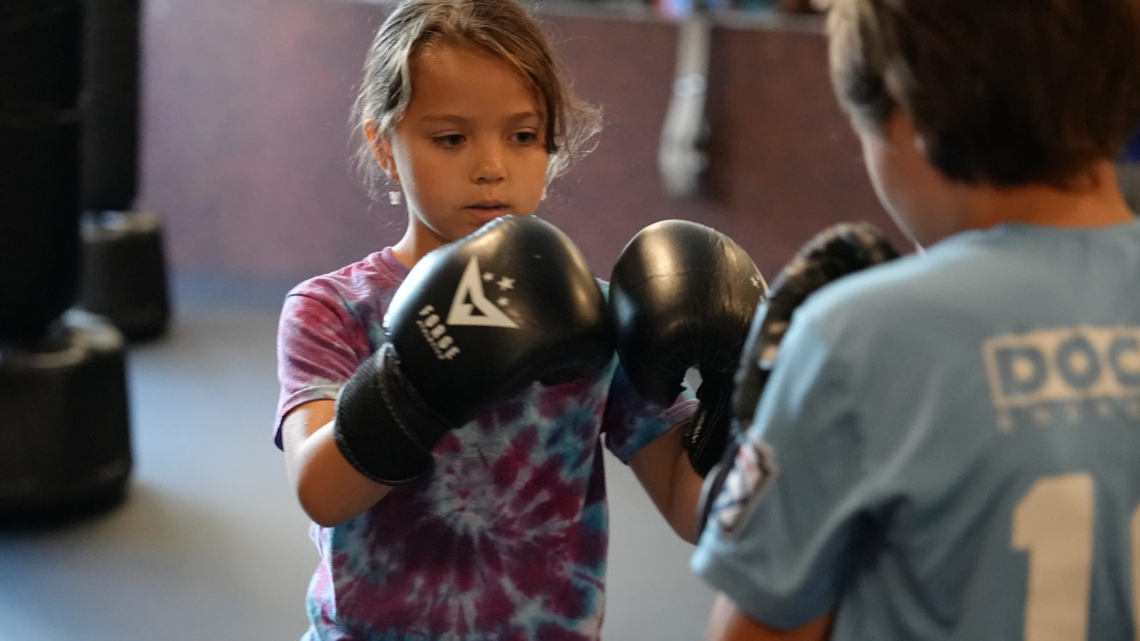 A young student holds her guard in boxing gloves while a coach teaches kids self-defense at Forge Athletics in Naples