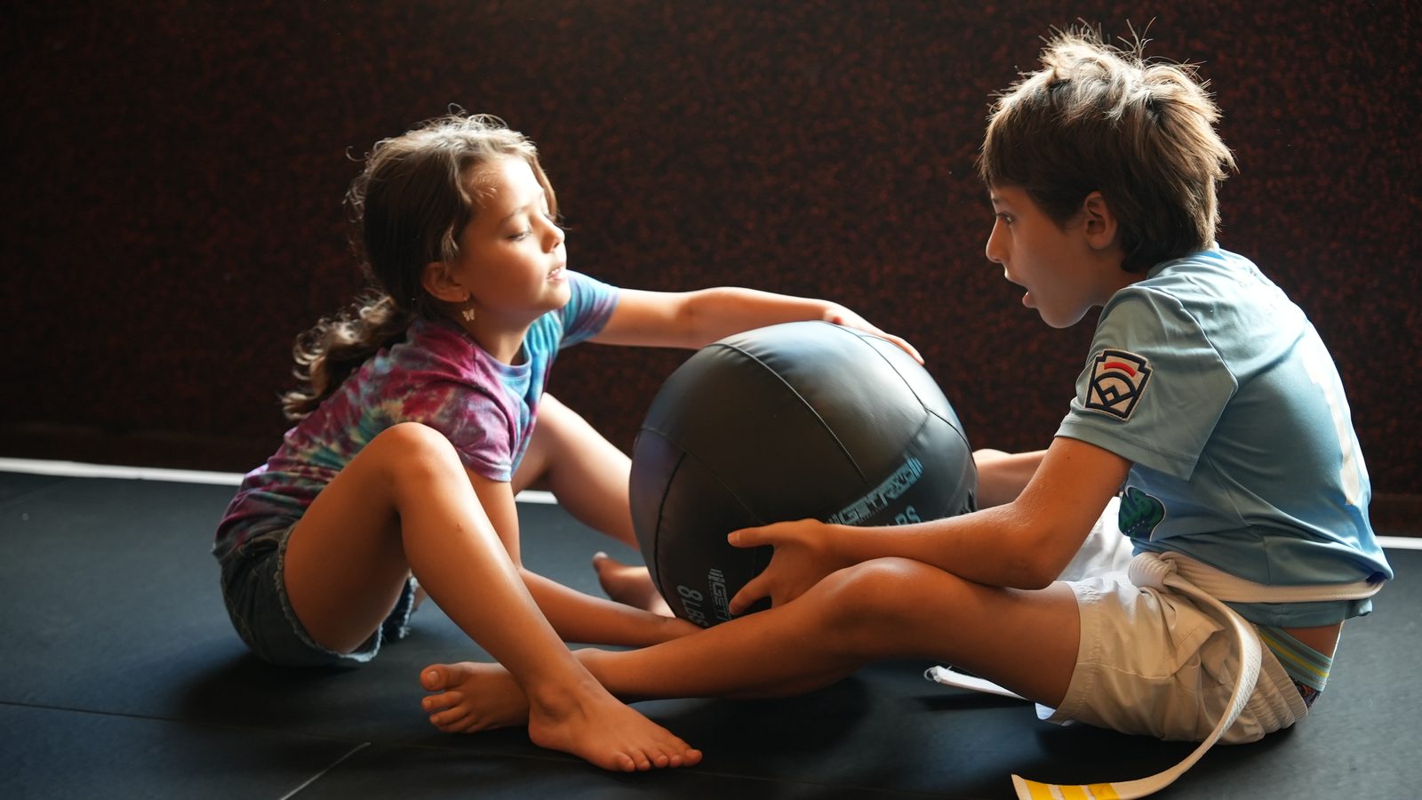 Two kids play a medicine ball game on the mat at Forge Athletics in Naples