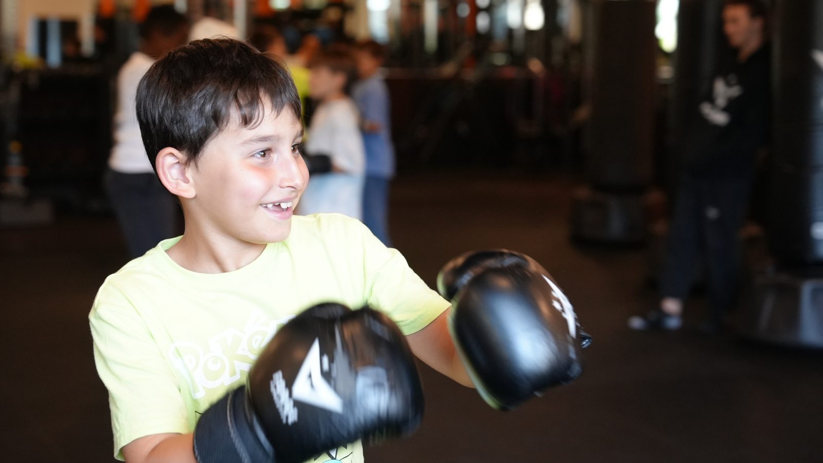 A Kids MMA student smiles mid-drill in boxing gloves at Forge Athletics in Naples
