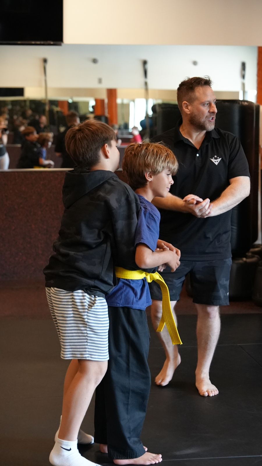 Coach Wil guides two young students through a partner drill on the Forge Athletics floor in Naples