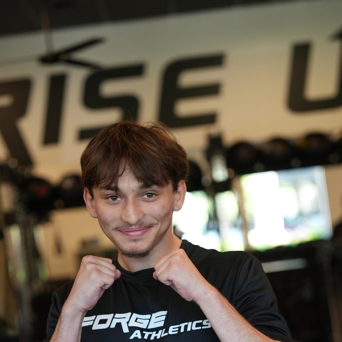 Coach Nikki smiling in front of the RISE UP wall at Forge Athletics in Naples