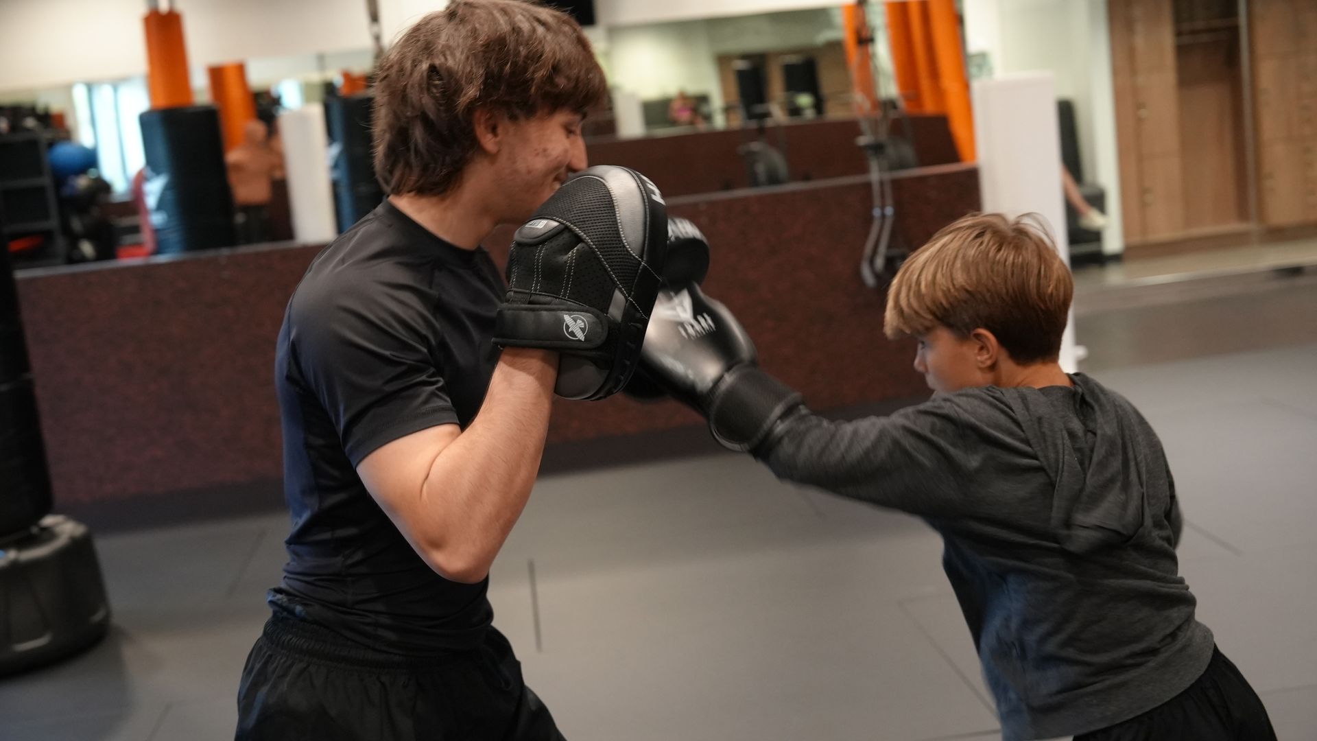A young athlete drives a punch into his coach's pads during a one-on-one kids personal training session at Forge Athletics