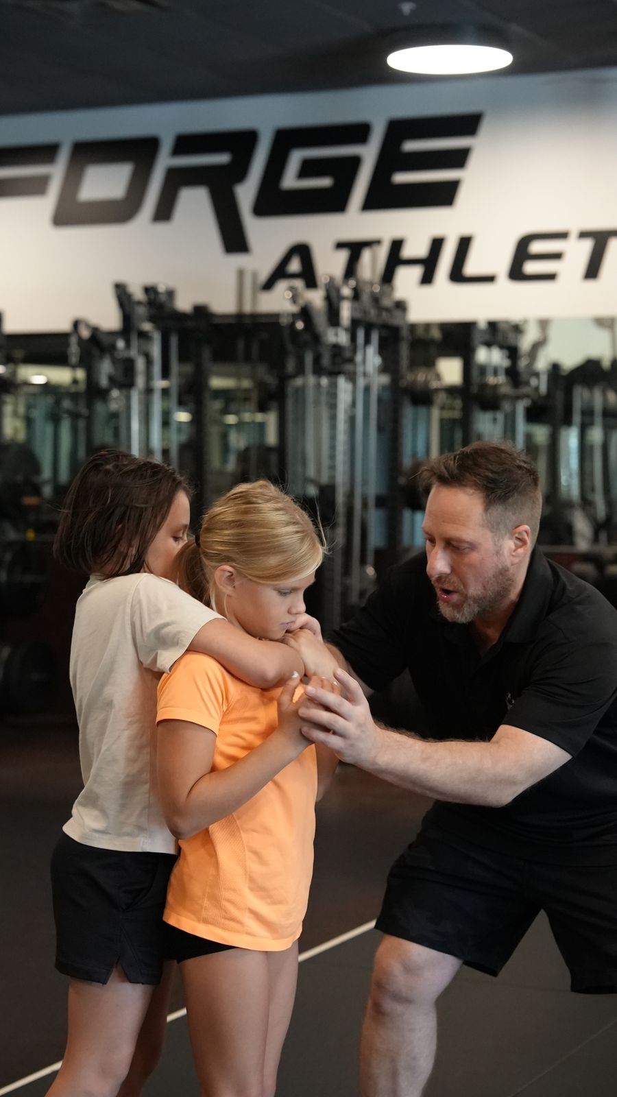 Coach Wil teaches two girls to break a rear grab in Kids Self Defense at Forge Athletics in Naples