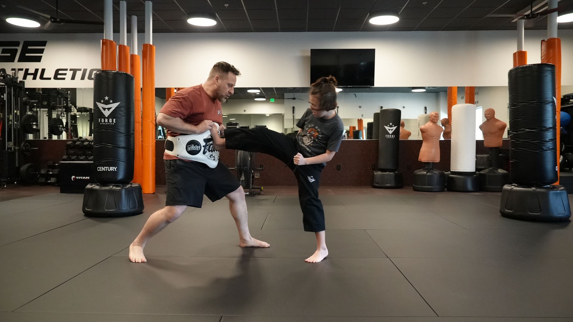 Coach Wil holds a striking shield for one client mid-kick on the Forge Athletics training floor in Naples