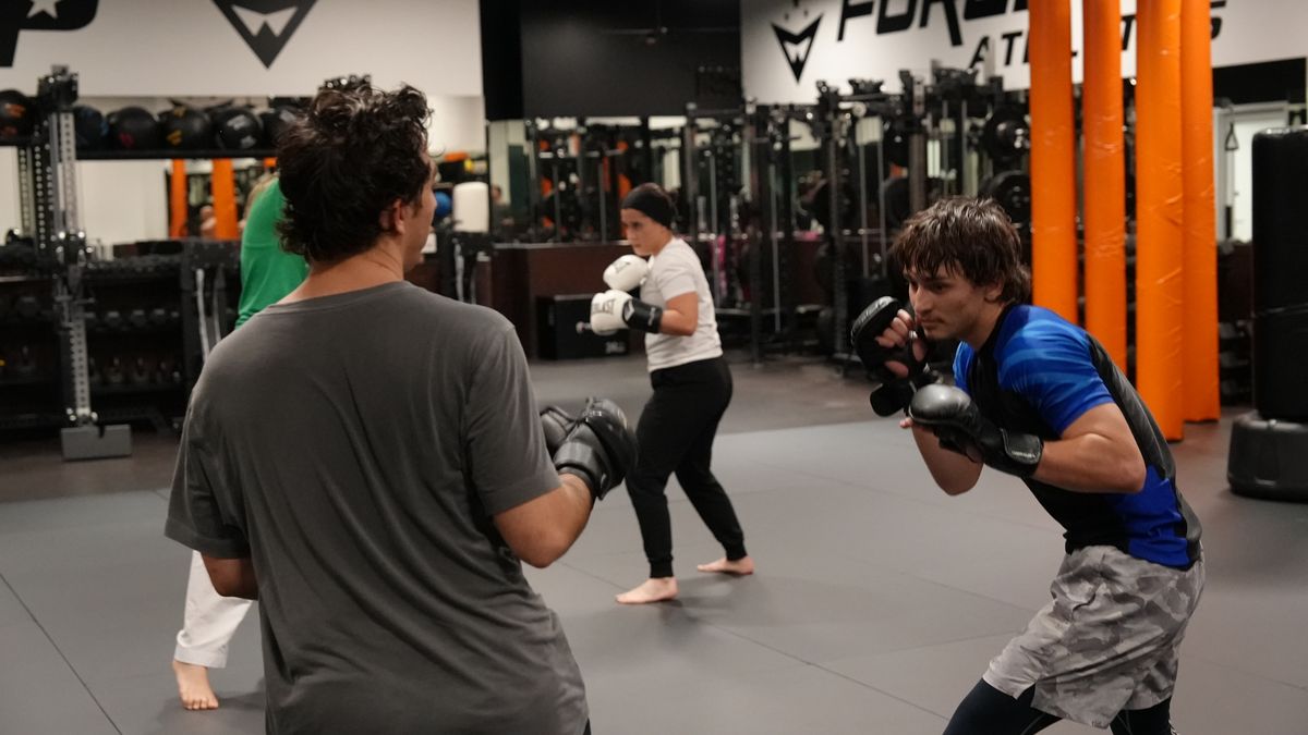 Adults in gloves square up for a coached partner striking round during MMA training at Forge Athletics in Naples