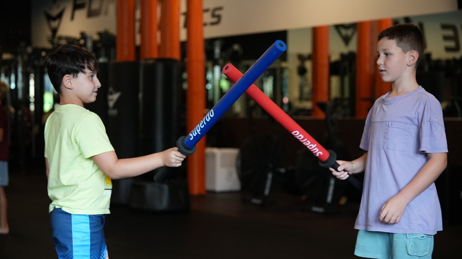 Two kids cross foam swords in a battle on the training floor at Forge Athletics in Naples
