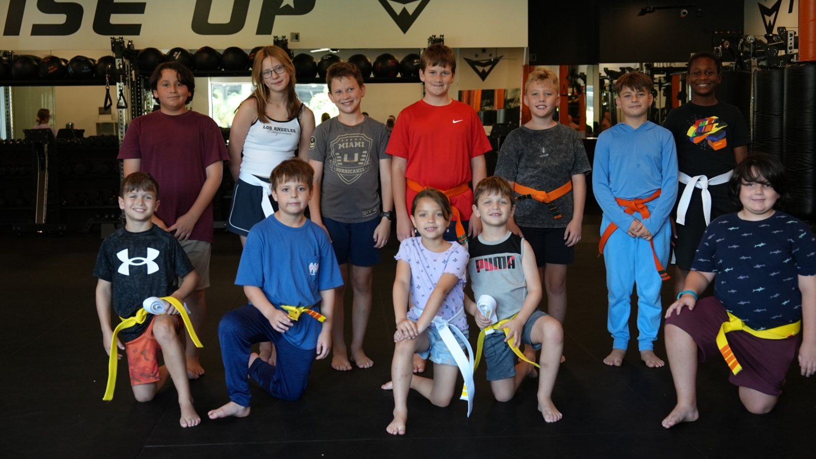 A group of kids in their new belts gather for a photo under the Rise Up wall at Forge Athletics in Naples