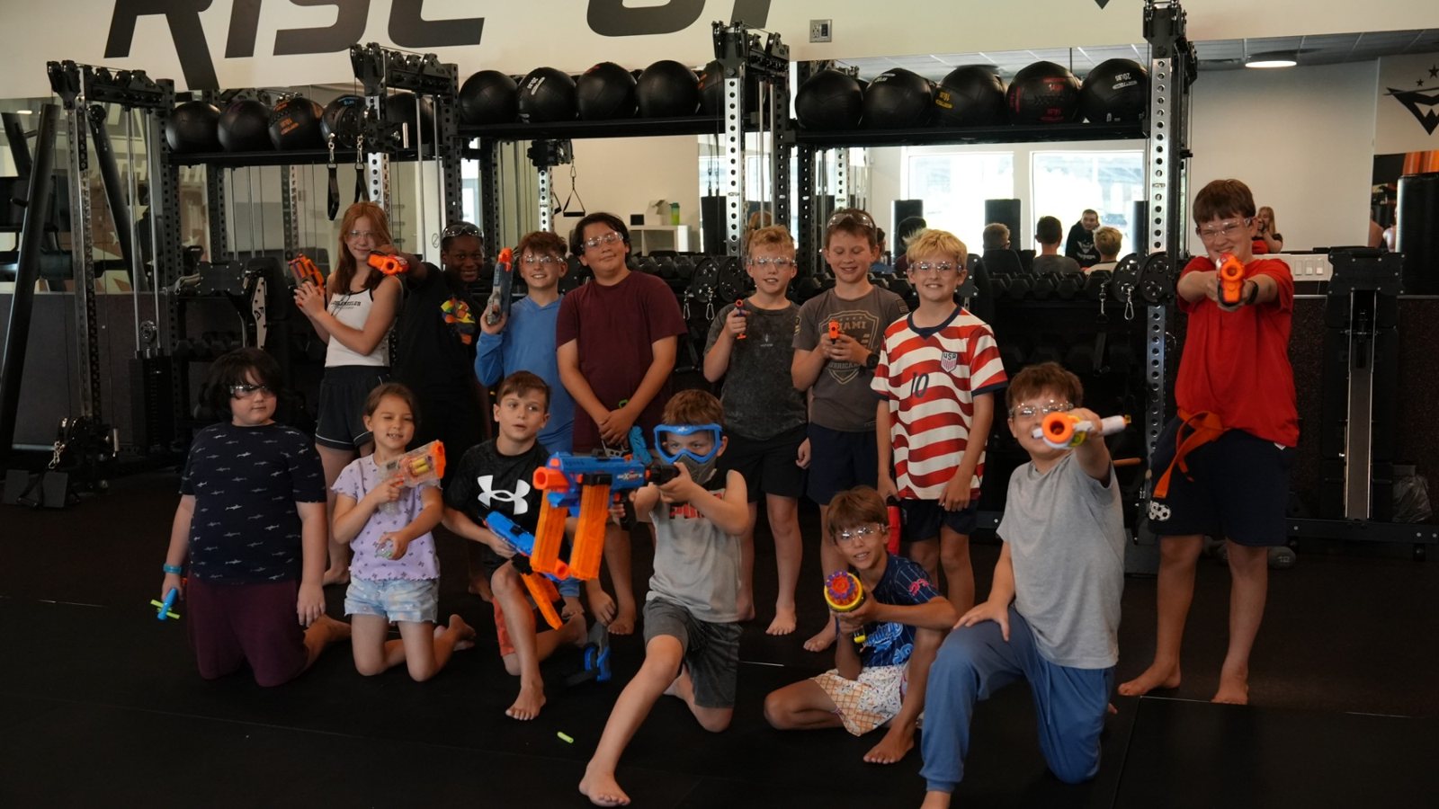 A group of kids in safety goggles pose with their Nerf blasters on the mat at Forge Athletics in Naples