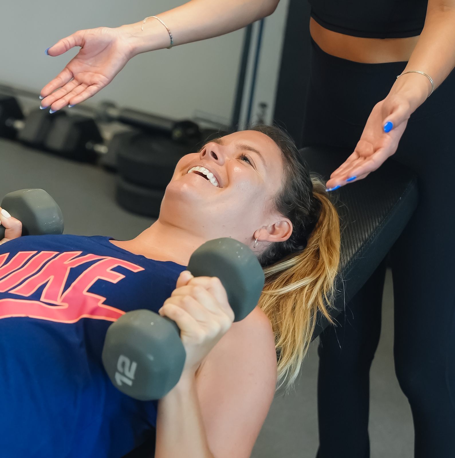A member laughs mid-set as her coach spots a dumbbell press during personal training at Forge Athletics in Naples