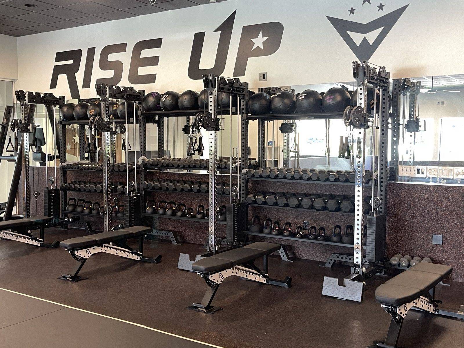 The strength floor with racks, benches and dumbbells under the Rise Up wall at Forge Athletics
