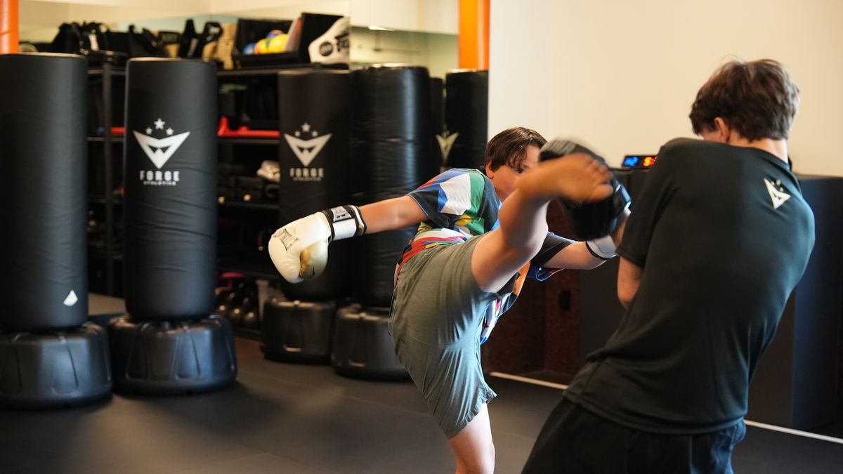 A teen lands a high roundhouse kick on a Forge Athletics bag during Youth MMA training in Naples