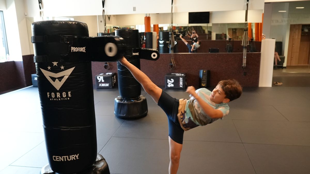 A young athlete throws an explosive high kick at a free-standing bag at Forge Athletics
