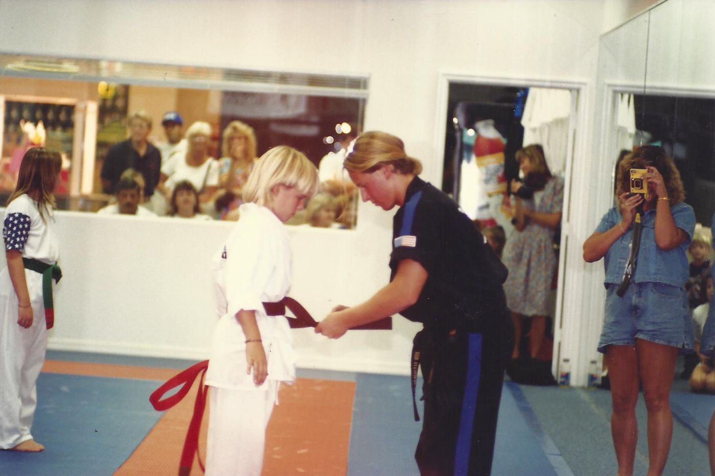 Sixteen-year-old Wil Pino ties a new belt on a young student at the Coastland Center mall dojo