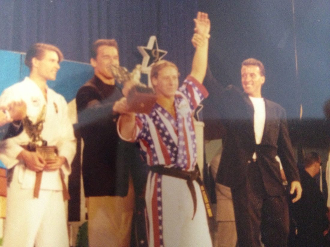 Arnold Schwarzenegger raising Wil Pino's hand on stage after his Arnold Classic martial arts championship win in 1997
