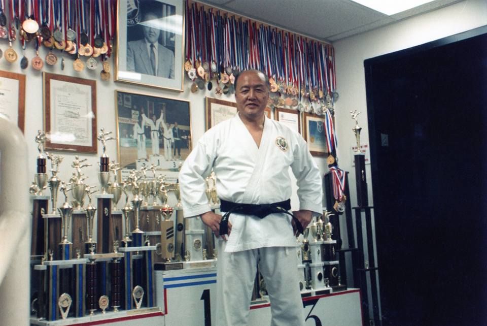 Grand Master Choi standing in front of his students' wall of medals and trophies