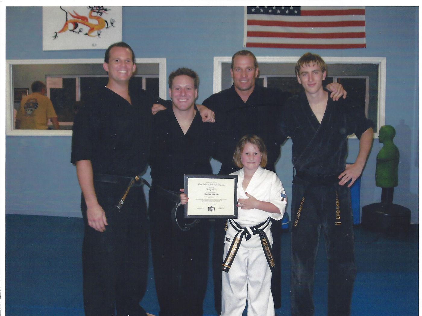 Wil Pino and his assistant coaches with a young student holding her black belt certificate at Elite Martial Arts