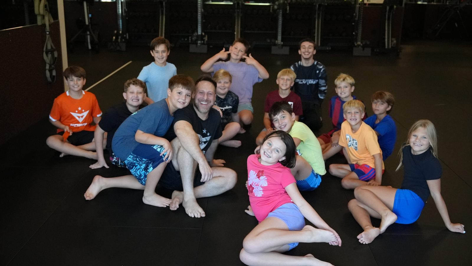 Coach Wil and Coach Nikki smiling with the whole kids class on the mats at Forge Athletics in Naples