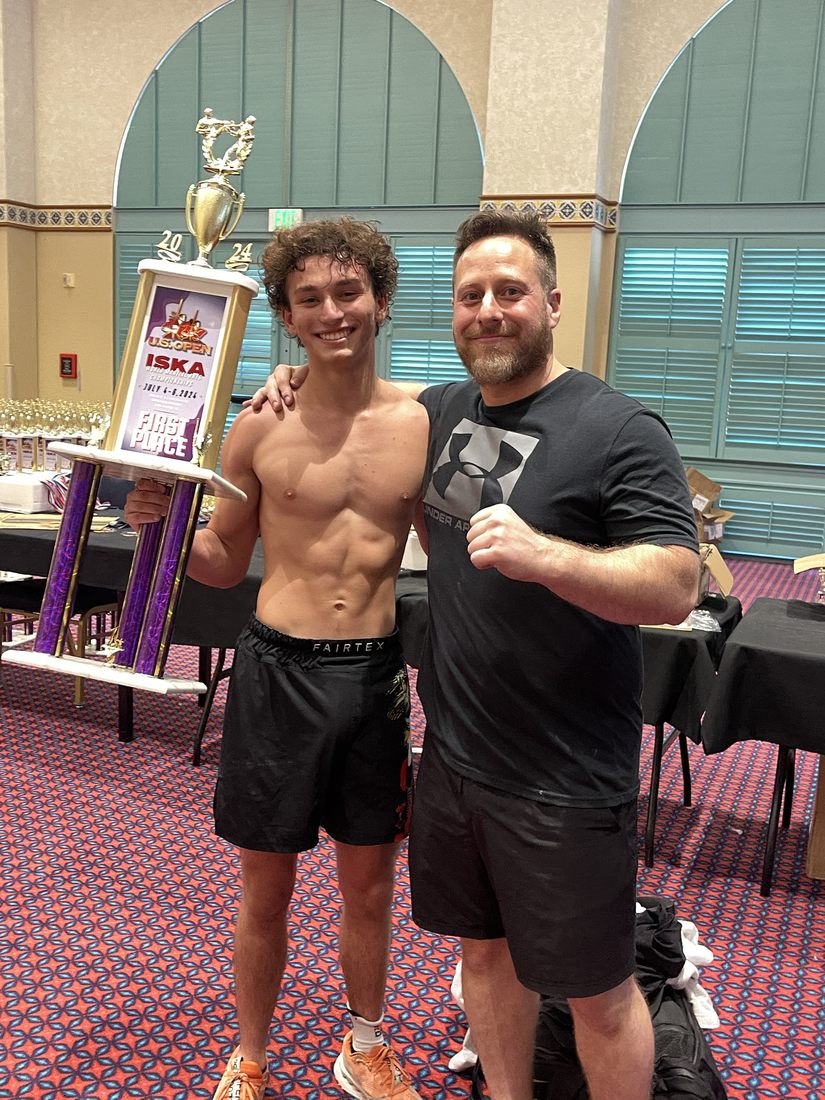 Coach Nikki holding his first-place US Open ISKA trophy beside Sensei Wil in 2024